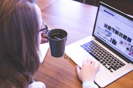 Woman drinks coffee and uses laptop.